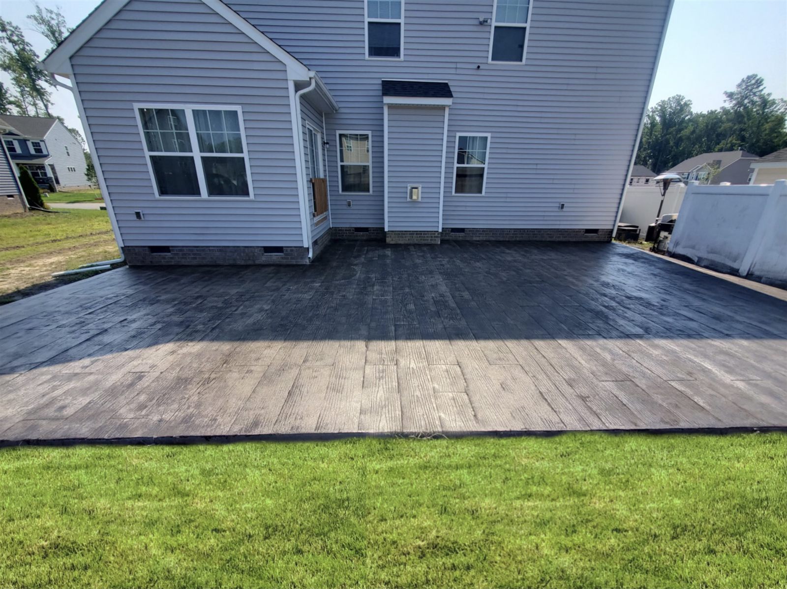 Stamped concrete patio with wood-plank finish behind a two-story home